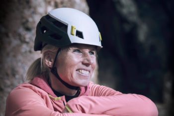 Eine lächelnde Frau mit dem Mammut Wall Rider MIPS Kletterhelm auf dem Kopf.