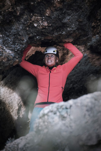 Eine Frua mit Kletterhelm stützt sich mit den Händen von unten gegen einen Felsvorsprung.