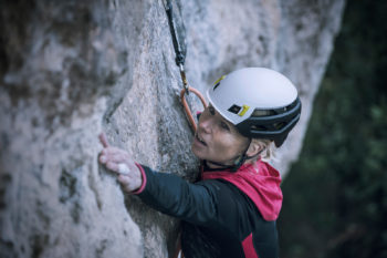 Eine Kletterin mit Helm konzentriert am Fels