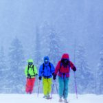Drei Skitourengeher in farbenfroher Skikleidung laufen durch verschneite Winterlandschaft