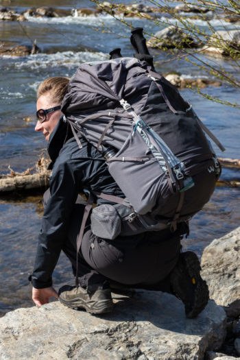 Frau mit Gregory Maven auf dem Rücken kniend am Fluss