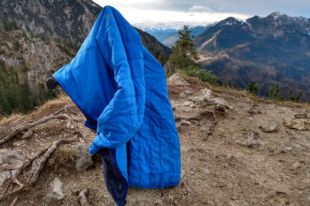Die Icebreaker Hyperia Lite Hybrid Jacke hängt auf einem Ast am Berg.